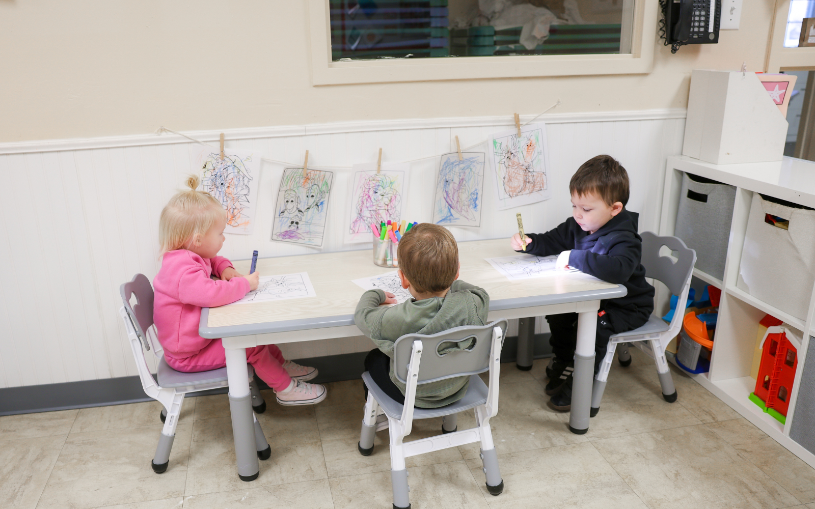 Teacher welcoming a parent and young toddler at the classroom entrance